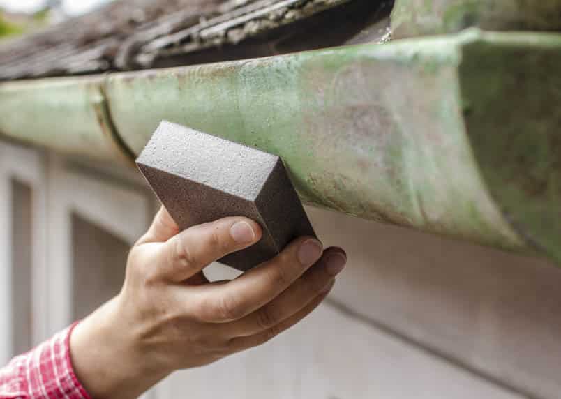 A man using a scrubbing brick to clean a copper or zinc gutter with patina.