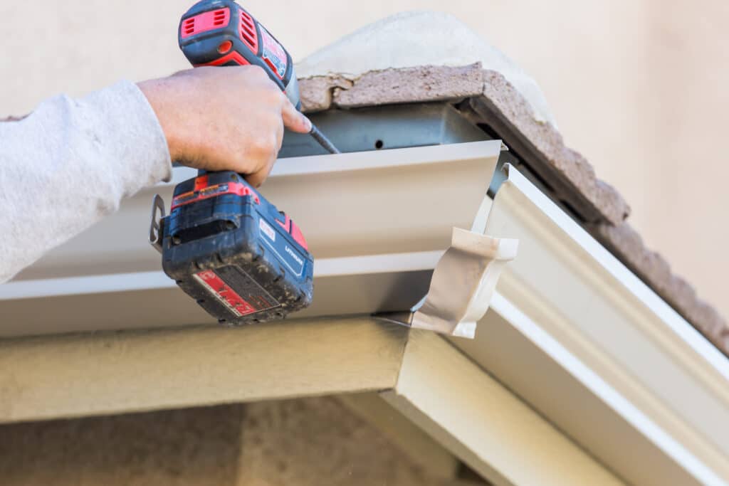 Installing a metal gutter with a drill.