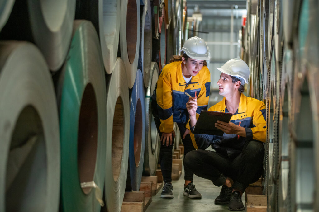 Two engineers checking metal coils in a sheet factory warehouse.