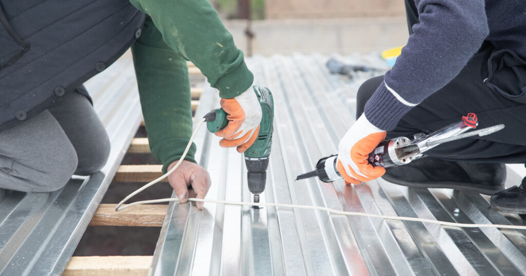 Man installing metal sheet roof with electric drill.