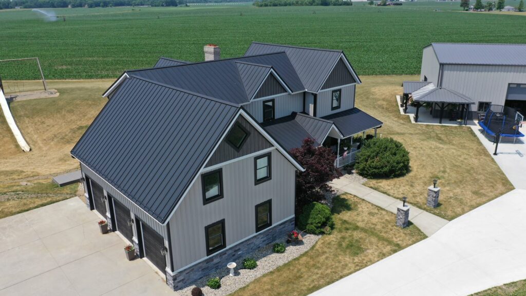 A metal board and batten farmhouse in an agricultural setting with a green field behind it.