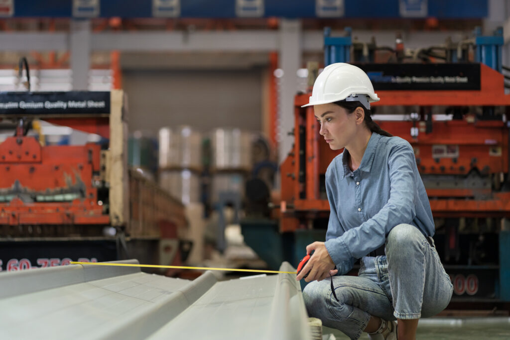 Metalwork manufacturing in plant. Female factory worker inspecting quality galvanized sheet or metal sheet in factory during manufacturing process. Female inspector checking metal sheet at warehouse