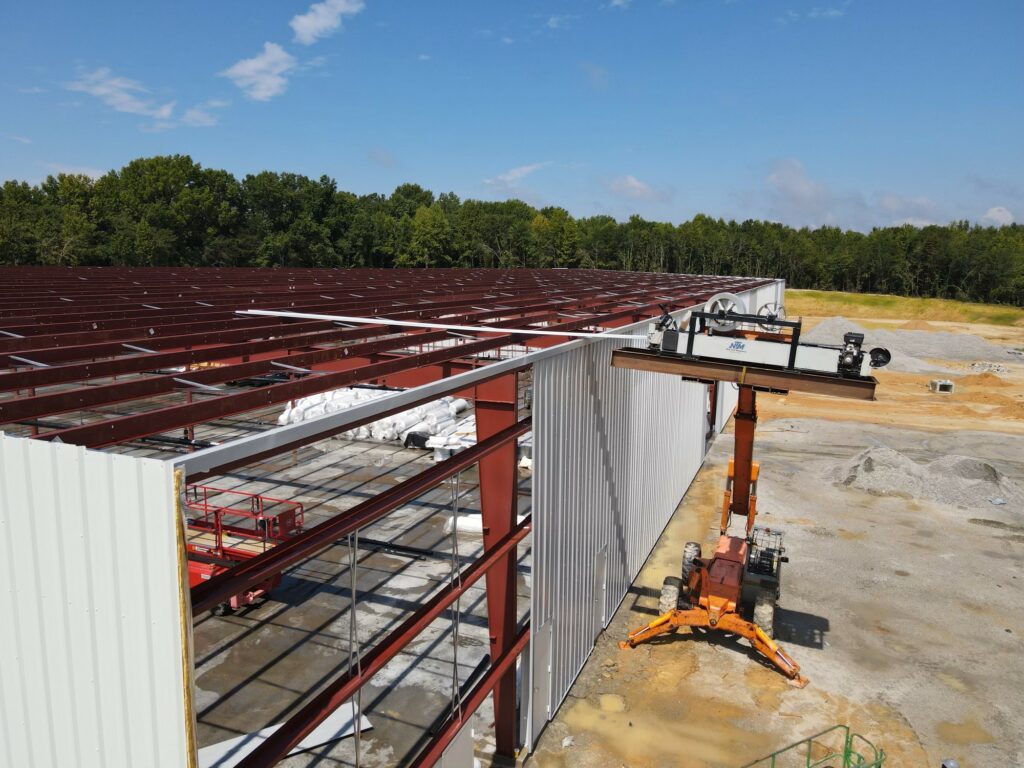 Rollformer lifted to roof level and fabricating a panel on top of an industrial building.